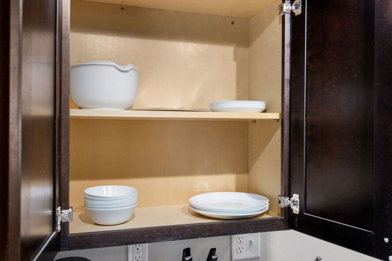 A kitchen cabinet with two shelves, each holding white bowls and plates.