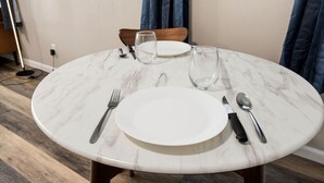 Una mesa redonda de mármol con un plato blanco, un tenedor, un cuchillo y una cuchara.