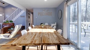 A modern living room with a wooden dining table, white chairs, a sofa, and a staircase. - Pocono Lake Charmer: Lakeview Retreat for 10 (Tobyhanna)
