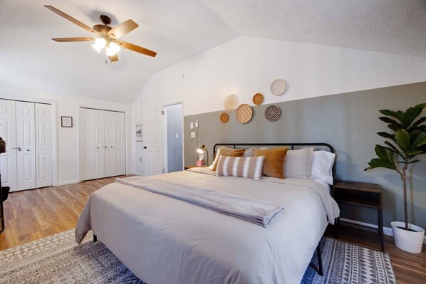 A bedroom with a bed, a ceiling fan, a nightstand, a potted plant, and a wall with decorative plates.