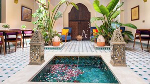 A luxurious indoor pool area with a tiled floor, surrounded by ornate furniture and tropical plants. - RIAD KECH ONE & SPA (Marrakech)
