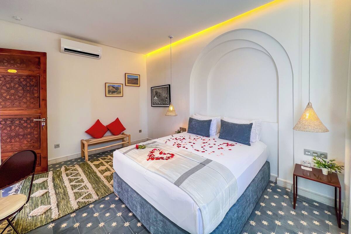A modern hotel room with a neatly made bed, a small seating area, and a decorative wall.