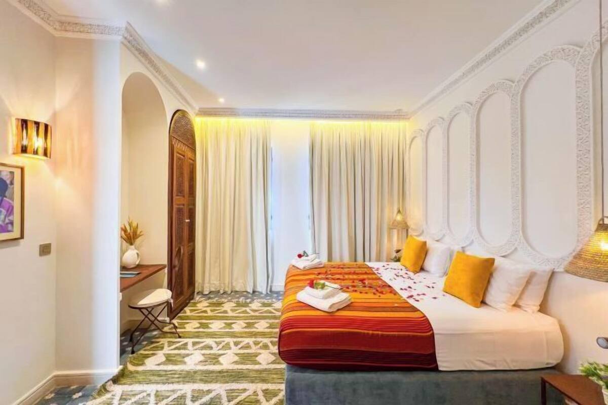 A hotel room with a bed, a desk, a chair, a wardrobe, and a patterned floor.