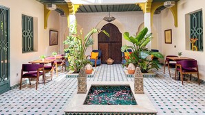 A courtyard with a fountain, seating areas, and a balcony with decorative railings. - RIAD KECH ONE & SPA (Marrakech)