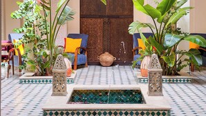 A courtyard with a fountain, tiled floor, and seating area with chairs and cushions. - RIAD KECH ONE & SPA (Marrakech)
