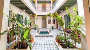 A courtyard with a tiled floor, potted plants, a small pool, and a balcony with railings. - RIAD KECH ONE & SPA (Marrakech)