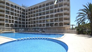 Et hotel med flere etager, et centralt poolområde, altaner på hver etage og en palme i forgrunden.