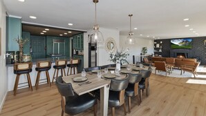 A modern kitchen with teal cabinets, a dining area with a wooden table and black leather chairs, and a living room with a fireplace and leather sofas. - Soaker Tubs + Decks | 5BR | Sleeps 12 (Lake Arrowhead)