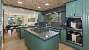 A modern kitchen with teal cabinetry, a central island, and built-in ovens. - Soaker Tubs + Decks | 5BR | Sleeps 12 (Lake Arrowhead)