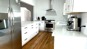 A modern kitchen with stainless steel appliances, wooden flooring, white cabinetry, and a coffee machine.