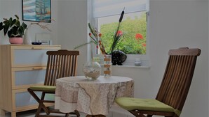 A dining area with a round table, two wooden chairs, a potted plant, and a window with a view of greenery. - Ferienwohnung Sommergluck in Proseken (Gaegelow)