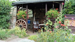 A rustic wooden structure with a porch, a large wooden wheel, and various hanging plants. - Ferienwohnung Sommergluck in Proseken (Gaegelow)