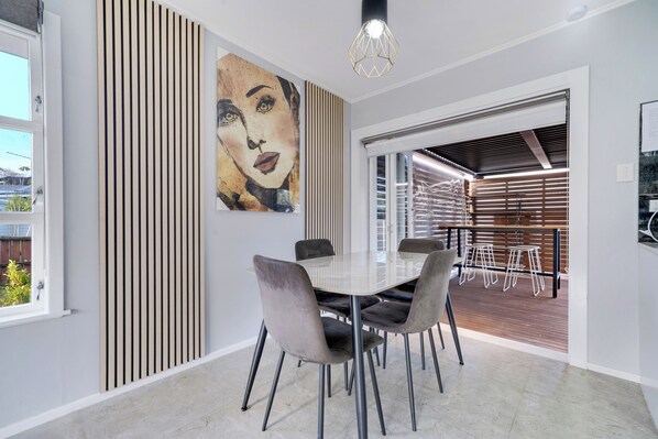 Un espace repas moderne avec une table blanche, des chaises à revêtement gris et un grand tableau abstrait accroché au mur.