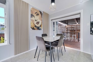 A modern dining area with a white table, grey upholstered chairs, and a large abstract painting on the wall.
