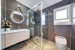 A modern bathroom with a glass-enclosed shower, a white sink, and a large mirror with circular lights.