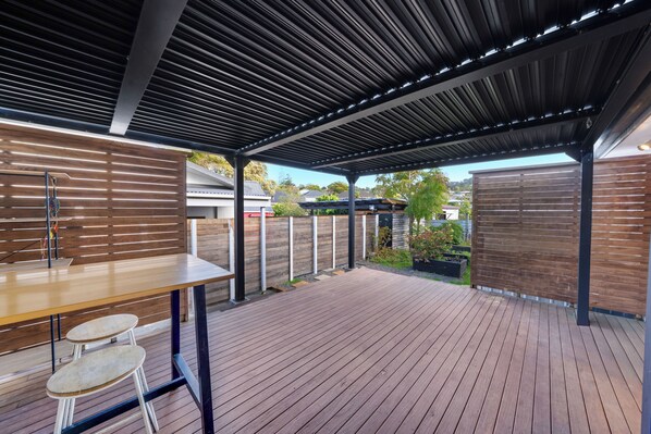 An outdoor patio with a wooden deck, metal-framed table, and chairs.