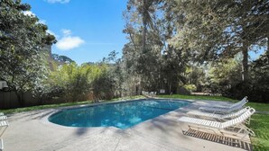 Piscina con sillones de descanso y un área verde con árboles.