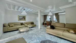 A spacious living room with a beige sofa, a coffee table, and a dining area in the background. - BLUE SKY SIDI BOUSAID (Carthage)