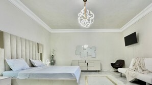 A modern bedroom with a large bed, a white sofa, a TV, and a decorative wall piece. - BLUE SKY SIDI BOUSAID (Carthage)