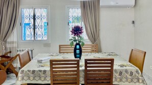 A dining area with a table set for four, surrounded by wooden chairs. There is a vase with flowers on the table, and a ceiling light fixture above. - BLUE SKY SIDI BOUSAID (Carthage)
