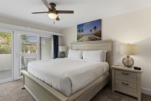 A bedroom with a bed, a nightstand, a ceiling fan, a painting, and a view through the glass door.