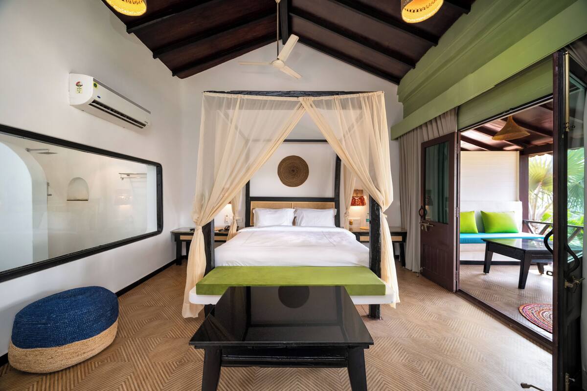 Un dormitorio con cama, mesita de noche, espejo, ventilador de techo y vistas a un área de estar exterior.