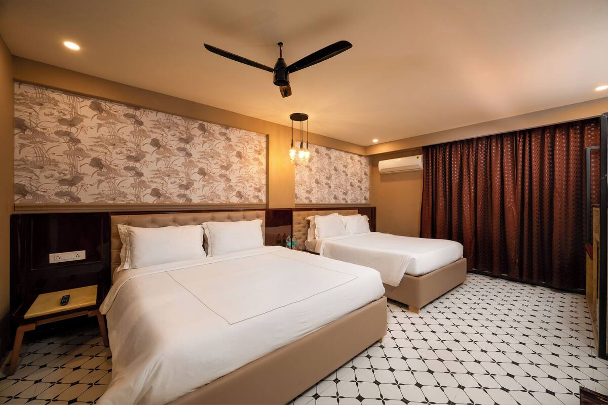 Una habitación de hotel con dos camas, ventilador de techo, papel tapiz estampado, candelabro y piso de baldosas.