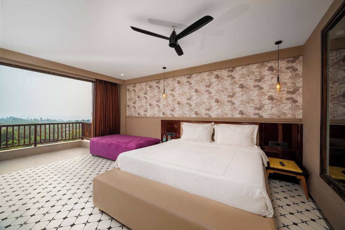 Habitación de hotel con una cama grande, un ventilador de techo, un balcón con vistas y una pared con diseño.