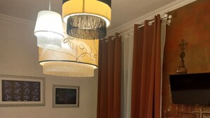 A hotel room with a bed, a chandelier, a television, and a painting on the wall. - Quadruple Comfort (Roma)