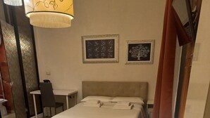 A hotel room with two beds, a desk, a chair, and two framed pictures on the wall. - Quadruple Comfort (Roma)