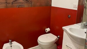 A bathroom with a red and white color scheme, a white sink, a bidet, and a toilet. - Quadruple Comfort (Roma)