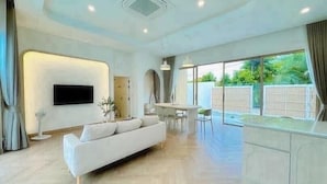 A modern living room with a sofa, a dining area, and a TV mounted on the wall. - Level TWO pool villa Sriracha (Si Racha)