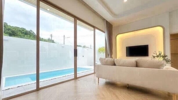 A modern living room with a large window, a pool, and a flat-screen TV mounted on the wall. - Level TWO pool villa Sriracha (Si Racha)