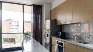 A modern kitchen with wooden cabinets, a stainless steel refrigerator, and a large window overlooking a cityscape.