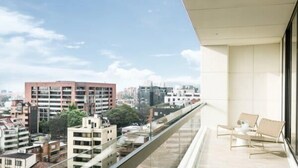 A balcony with a city view, a glass railing, and two wicker chairs.