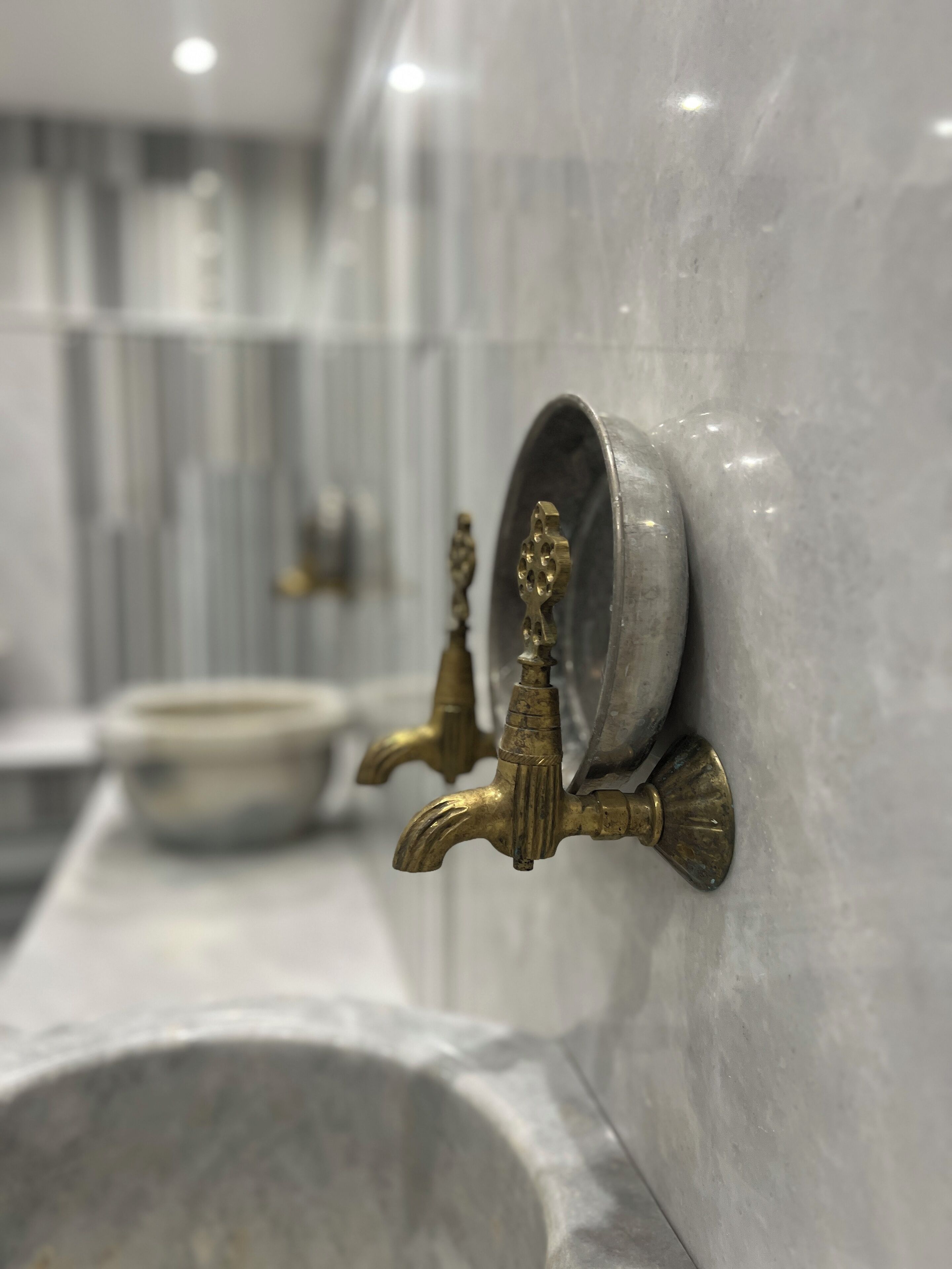 Un baño con paredes de mármol, un lavamanos e instalaciones de latón.