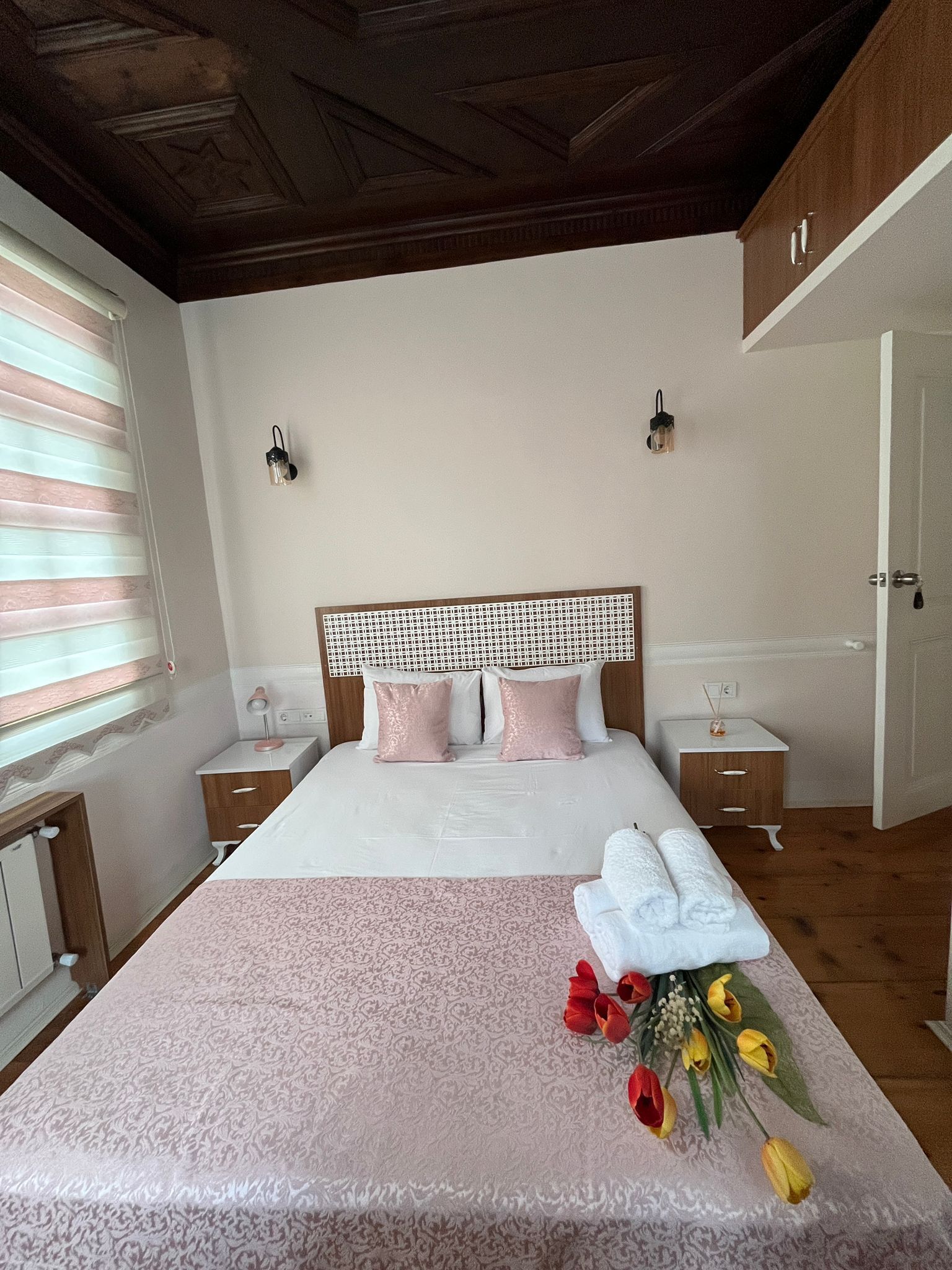 Une chambre à coucher comprenant un lit, des tables de chevet, une commode, une fenêtre avec des stores et une porte.