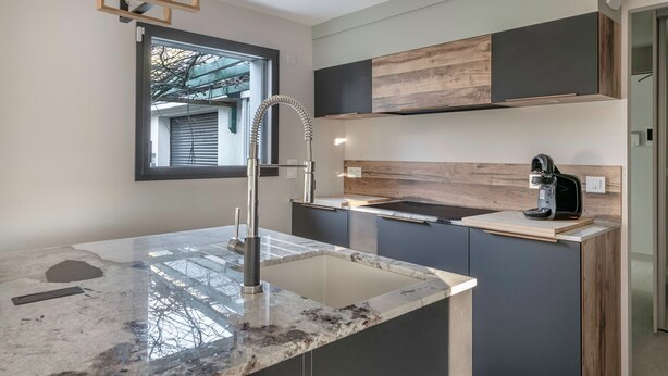 A modern kitchen with a marble countertop, stainless steel faucet, and a built-in coffee maker.