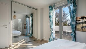 A bedroom with a large bed, a sliding glass door leading to a balcony, and a view of the outdoors.