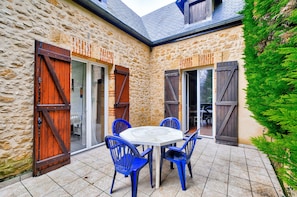 A stone building with a patio area featuring a round table and blue chairs. - Stone house with a terrace, ideal for 4 people (Sarlat-la-Canéda)