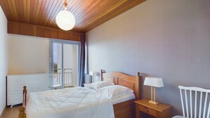 A bedroom with a wooden ceiling, a bed with white bedding, a nightstand with a lamp, and a white chair.