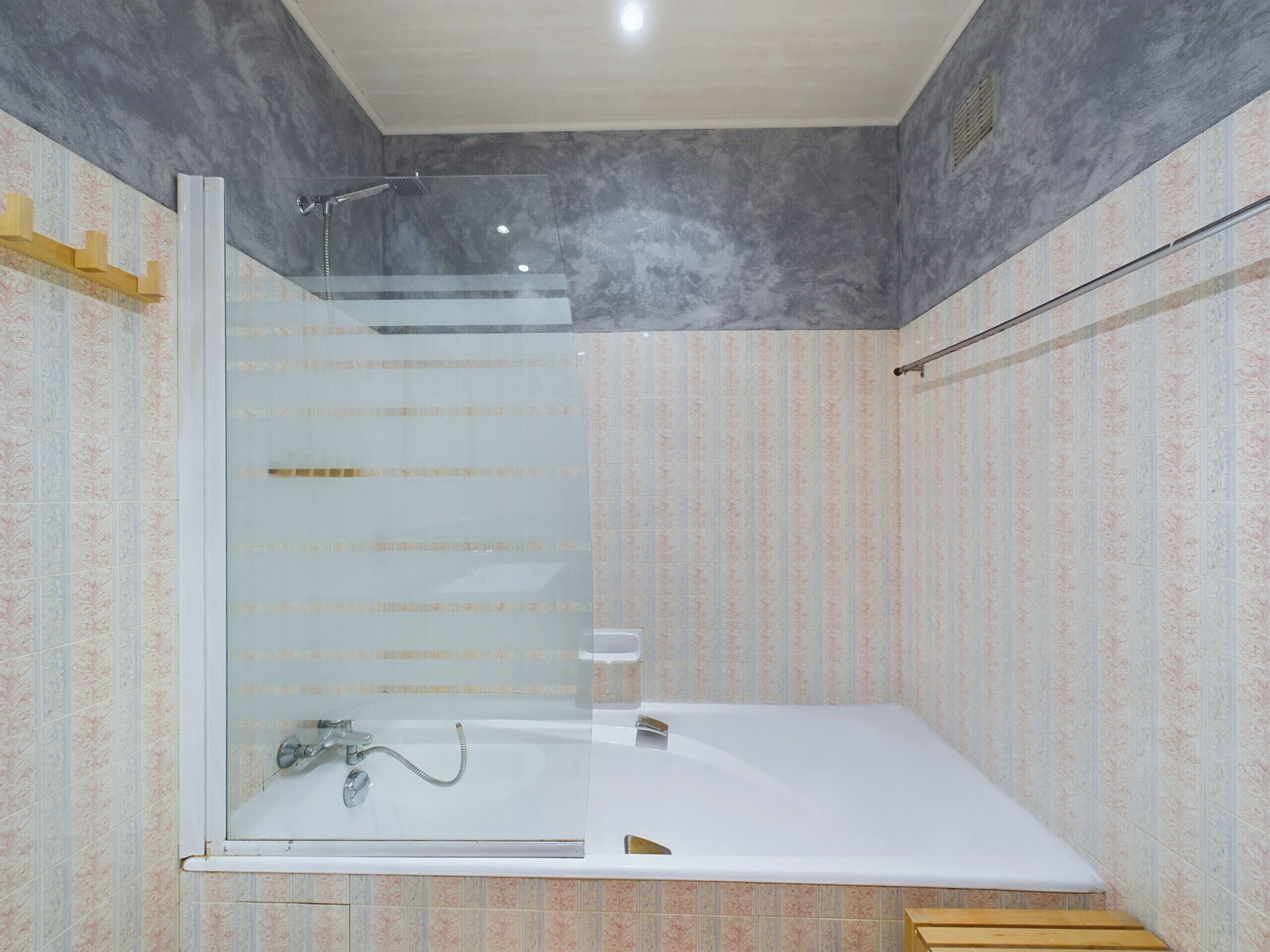A modern bathroom with a glass-enclosed shower, a freestanding bathtub, and patterned wallpaper.