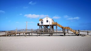 Una casa de playa con terraza de madera y una escalera que lleva a la entrada.
