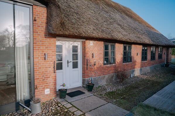 A brick building with a thatched roof, a white door, and potted plants at the entrance.