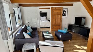 Un espacio habitable pequeño con sofá, reposapiés, mesa de centro, cama, televisor y puerta de madera.