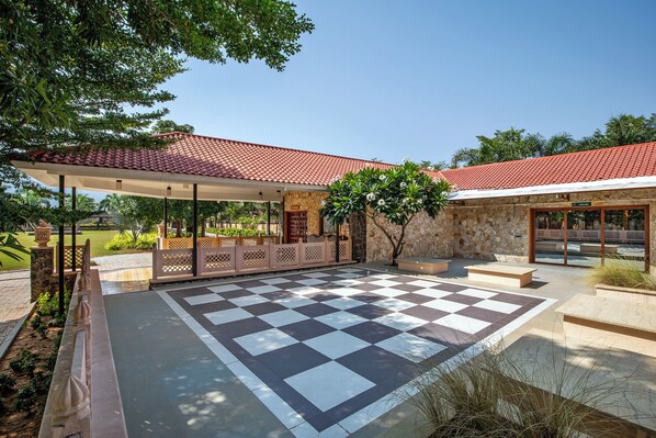 A covered outdoor area with a checkered floor, stone walls, and a red-tiled roof. - Vikrama Heritage Resort Pavagadh (Halol)