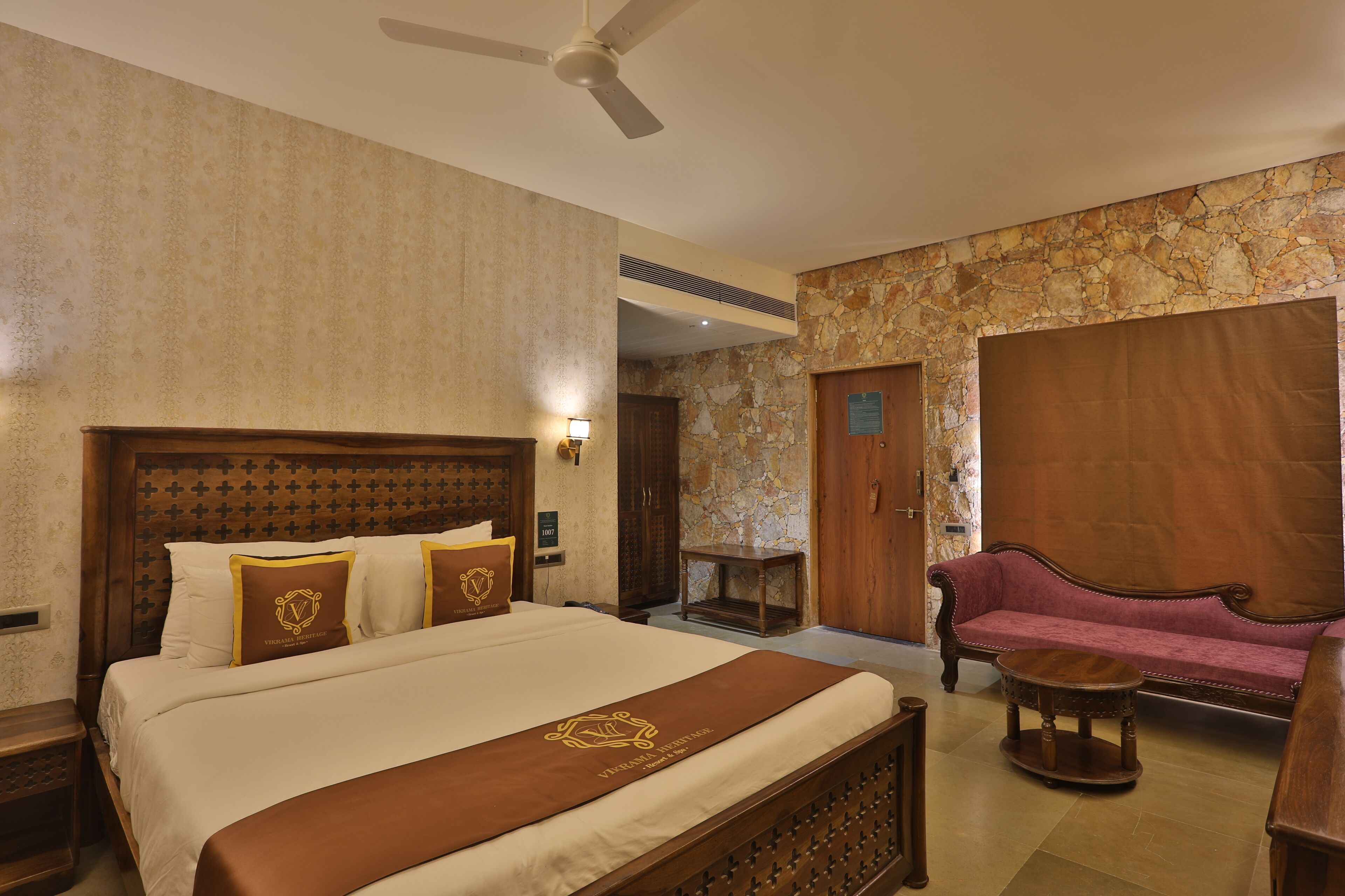 A hotel room with a large bed, a wooden headboard, a sofa, a small round table, and a ceiling fan.