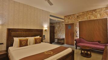 A hotel room with a large bed, a wooden headboard, a sofa, a small round table, and a ceiling fan.