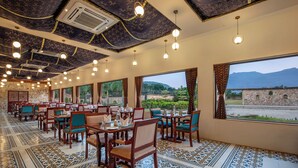 A restaurant with a long dining area, large windows, and a patterned floor. - Vikrama Heritage Resort Pavagadh (Halol)