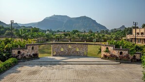 A paved area with a stone wall and arched openings, surrounded by greenery and a mountainous backdrop. - Vikrama Heritage Resort Pavagadh (Halol)
